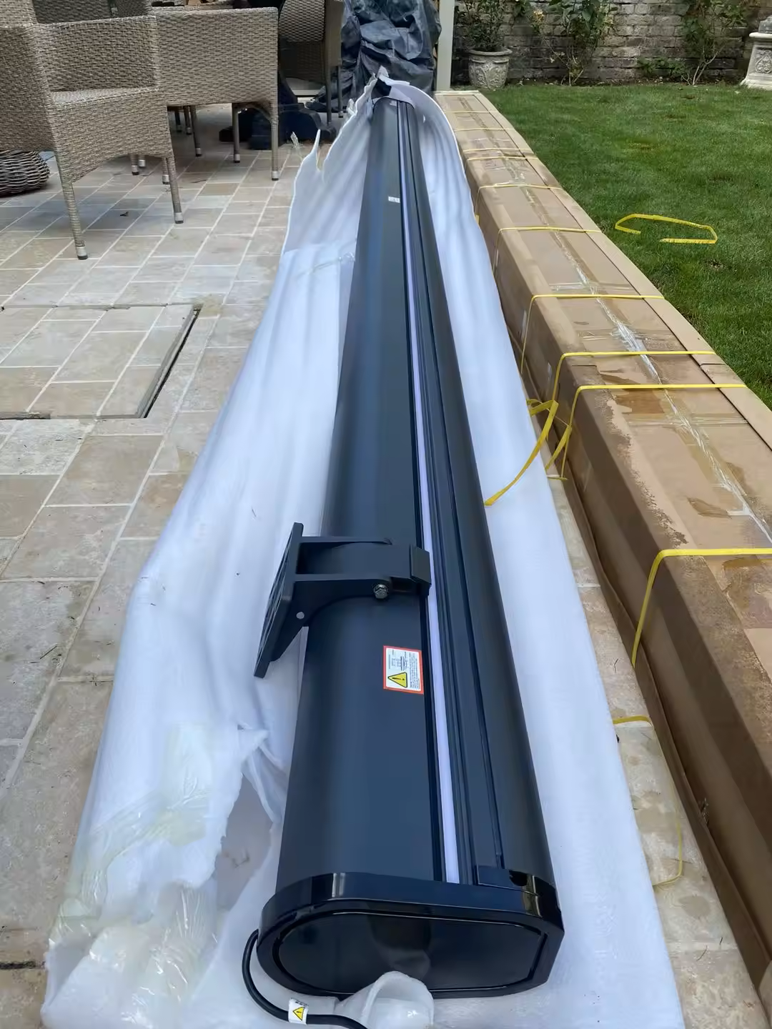 Motorized full cassette awning safely unboxed on a stone patio in the UK, ready for wall bracket installation