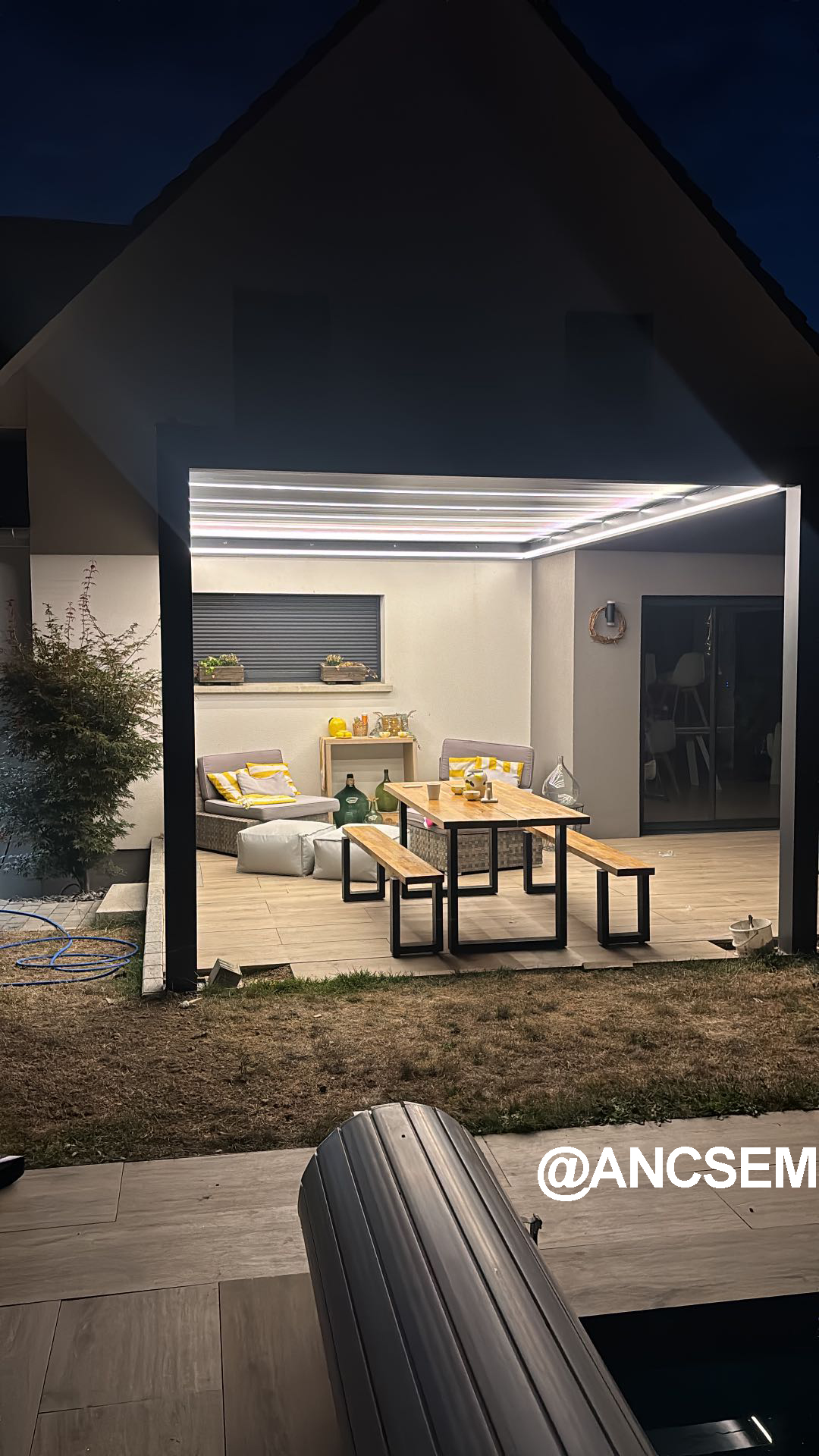 Wall-mounted louvered pergola illuminated at night by its integrated LED lighting in France
