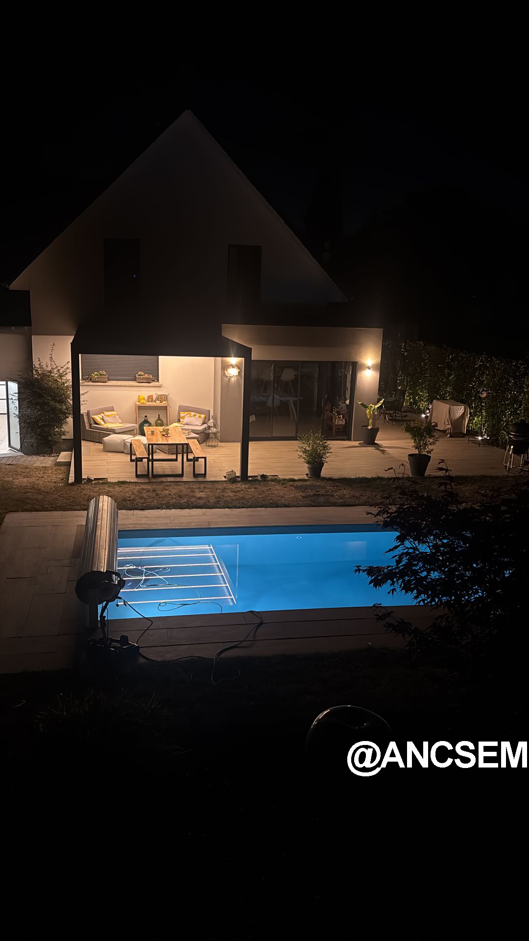 Wall-mounted louvered pergola beside a lit swimming pool at night in France