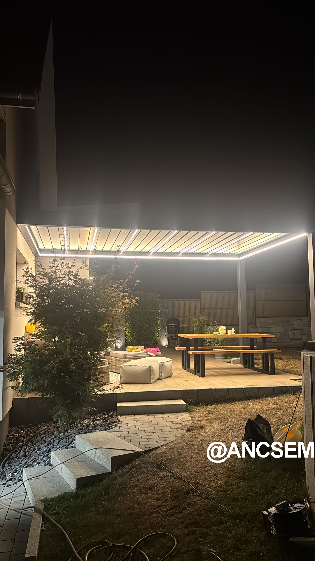 Dark grey wall-mounted pergola lighting a patio and steps at night in France