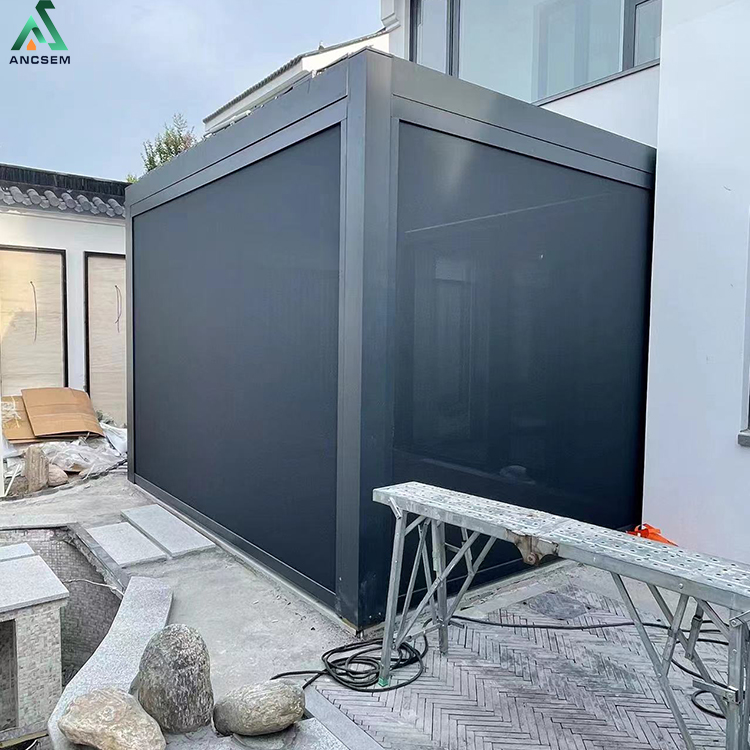 Black windproof roller blinds fully closed around an anthracite aluminium pergola frame, turning a patio into a sealed, weatherproof outdoor room