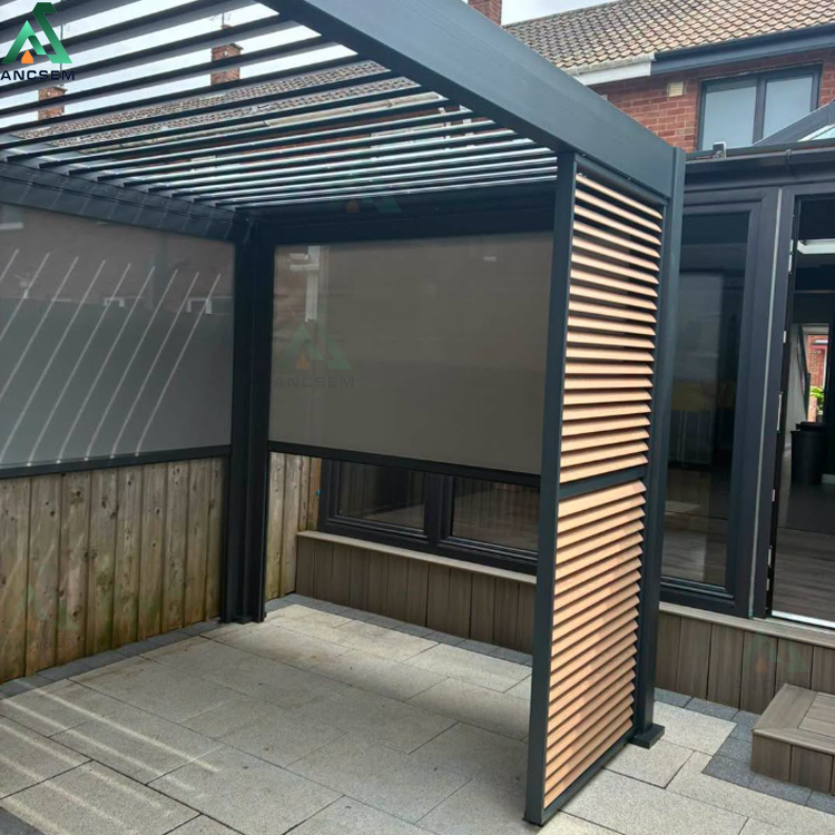 Anthracite aluminium louvered pergola with wood-effect privacy screen panels and grey roller blinds installed against a red brick UK house
